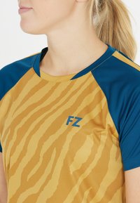 Lyhythihainen urheilupaita, jossa on kultapohja tiikerinraidallisella kuviolla, siniset hihat ja kontrastivärinen sininen "FZ" -logo.