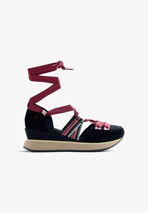 Sandale compensée noire avec des sangles roses qui s'enroulent autour de la cheville, des bandes élastiques multicolores sur le côté, et une semelle beige avec une bande de roulement noire.