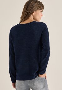 Granatowy sweter o teksturowanym wykończeniu, z długimi rękawami i okrągłym dekoltem. Posiada luźny krój oraz rozcięcia po bokach u dołu.