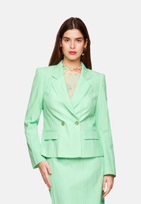 Mint green double-breasted blazer with vertical stripes, two front pockets, and structured lapels, worn over a patterned top.
