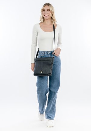 Černá kožená crossbody taška s minimalistickým designem, vybavená magnetickým uzávěrem a logem v zlatém odstínu. Hladká textura, obdélníkový tvar.