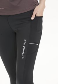 Svarta sportleggings med sidficka och vit "ENDURANCE" logotyp. Snygg, figurnära design med kontrasterande sömdetaljer.
