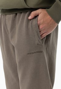 Pantaloni joggers gri din bumbac cu o croială lejeră, dotate cu buzunare laterale și un logo embosat pe coapsă. Textură moale, talie elastică.