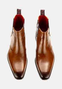 Braune Leder-Ankle-Boots mit spitzem Zeh, die eine kontrastierende schwarze Rückseite mit einer dekorativen Zuglasche und lebhaftem roten Futter aufweisen.