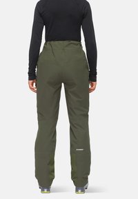 Gröna skidbyxor med hög midja, med fickor och texturerade nederdelar för ventilation, i kombination med svarta långärmade tröjor.