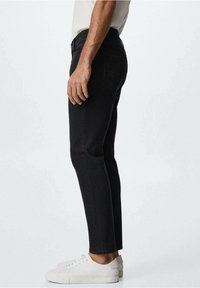 Jeans de mezclilla negra con un ajuste Slim, que cuentan con un diseño de cinco bolsillos y un sutileza en la costura. Combinados con zapatillas blancas para crear contraste.