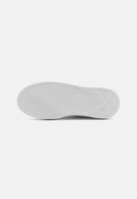 White rubber sneaker sole with a textured pattern, featuring a raised logo and smooth curves along the edges.