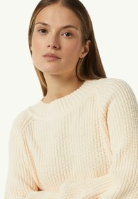 Helle beige Strickjacke mit geripptem Rundhalsausschnitt, strukturiertem Stoff und langen Ärmeln, mit einem lässigen Schnitt und subtilen Details.
