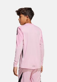 Maglietta sportiva a maniche lunghe di colore rosa chiaro, con dettagli neri sulle spalle e pannelli di tessuto testurizzato lungo le maniche.
