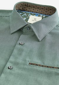 Green patterned shirt with a textured weave, featuring a brown accent on the pocket and a contrasting floral inner collar lining.