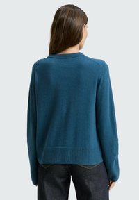 Türkisfarbener Strickpullover mit rundem Ausschnitt und geripptem Saum, langen Ärmeln und lockerer Passform. Glatte Textur und minimale Details.