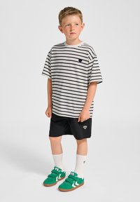 Randig kortärmad skjorta i vitt och marinblått, kombinerad med svarta shorts. Gröna sneakers med vita detaljer. Vita crewstrumpor.