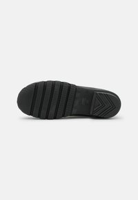 Black rubber shoe sole with textured grip pattern and groove lines; features a solid toe cap and angled heel for stability.