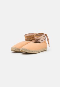 Sapatilhas espadrilles de cor pêssego claro com sola plana em corda entrelaçada e tiras metálicas envolvidas à volta do tornozelo.