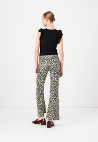 Haut noir à manches courtes avec des accents de volants, associé à un pantalon évasé beige arborant un imprimé léopard noir. Des chaussures marron complètent l'ensemble.