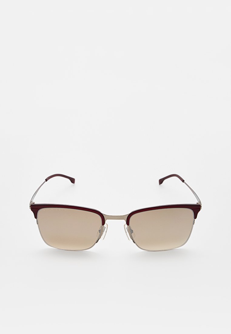 Rechteckige Sonnenbrille mit dunkelrotem Rahmen, braun getönten Gläsern mit Verlauf, metallischen Akzenten und Kunststoffbügeln in geschwungenem Design.