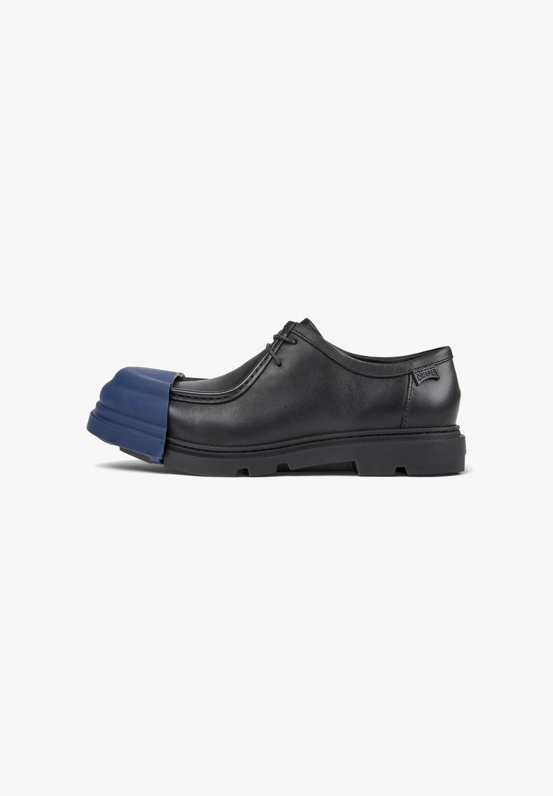 Scarpa nera con lacci e un unico copri punta in gomma blu, caratterizzata da una suola testurizzata e un design minimalista, esposta su uno sfondo bianco.