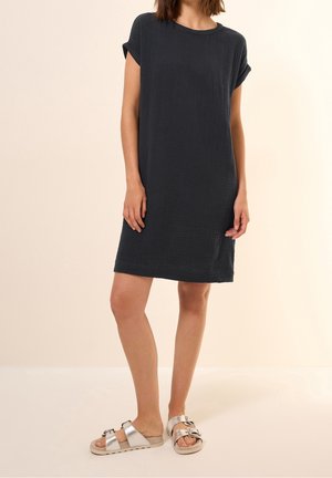 Ciemnoszara sukienka o krótkim rękawie do kolan, wykonana z teksturowanej tkaniny, zestawiona z metalicznie srebrnymi sandałami z dwoma klamrami.