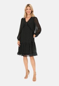 Czarna sukienka w kropki z dekoltem w serek, falbaniastym dołem i przezroczystymi długimi rękawami. Posiada kieszenie oraz lekką, teksturowaną tkaninę.
