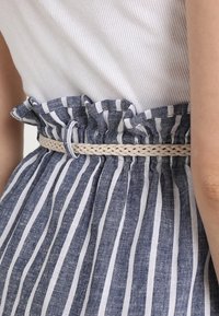 Modrá a bílá pruhovaná látka s volánkovým pasem a pleteným béžovým opaskem, která vykazuje texturovaný vzhled lnu.