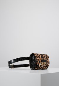 Syntetyczna torebka w panterkę z czarnym paskiem i detalami ze skóry lakierowanej. Posiada prostokątny kształt oraz złote zapięcie.