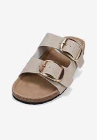 Sandal beige a scivolo con due ampie cinghie e fibbie dorate. Soletta morbida e suola in sughero, con una texture liscia e bordi arrotondati.