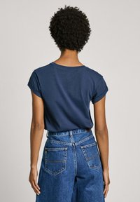 Camiseta azul marino con mangas enrolladas, mostrada desde la parte de atrás. Combinada con jeans de mezclilla de tiro alto que presentan bolsillos traseros y detalles de costura.