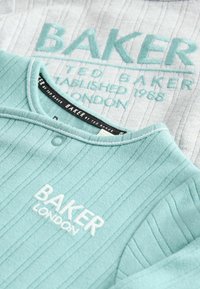 Jasnoniebieski prążkowany top z białym haftowanym logo "BAKER LONDON". Posiada guzik przy dekolcie i teksturowaną tkaninę. W tle szary top.