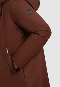 Brown, padded coat with a hood, featuring a circular black logo on the sleeve, and a side pocket with a label. Smooth texture and clean lines.