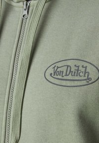 Hoodie zippé vert en tissu texturé avec un logo "Von Dutch" sombre sur le devant.