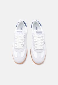 Ζευγάρι λευκών και ανοιχτό γκρι αθλητικών παπουτσιών με σόλες από καουτσούκ, λευκά κορδόνια, ναυτικού χρώματος λεπτομέρειες στη φτέρνα και ετικέτα της μάρκας στις γλώσσες, απεικονιζόμενα από πάνω.