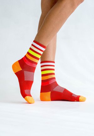 Bunte Sportsocken mit rotem Grund und vertikalen Streifen in Weiß, Gelb, Orange und Pink. Strukturierte Netz-Einsätze und orangefarbene Zehenakzente.