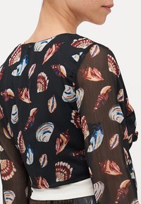 Blusa nera con maniche lunghe trasparenti, caratterizzata da un motivo a conchiglia nei colori rosso, blu e crema. Collo rotondo e vita aderente.