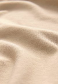 Beige stretchtyg med en slät textur, som visar upp fina stickade mönster och mjuka draperingar. Ytan verkar något reflekterande.