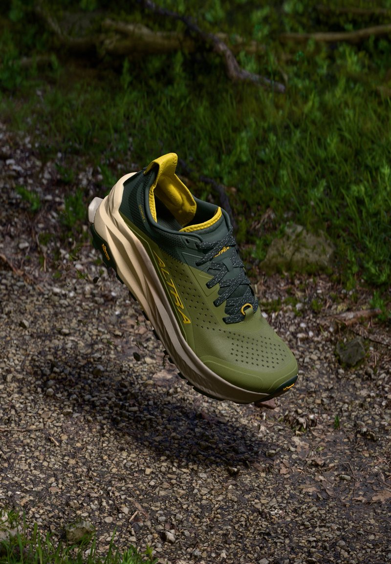 Chaussure de sport verte et jaune avec un dessus texturé, une semelle intermédiaire rembourrée et une semelle extérieure à motifs, conçue pour la course en sentier.