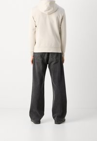 Jeans grigi oversized con vita alta e design a gamba larga, abbinati a una felpa color crema con cappuccio regolabile.