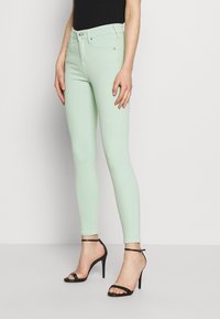 Světle modré skinny jeans z denimu, s vysokým pasem, pěti kapsami a zapínáním na knoflík, doplněné černými sandály na vysokém podpatku se strapci.