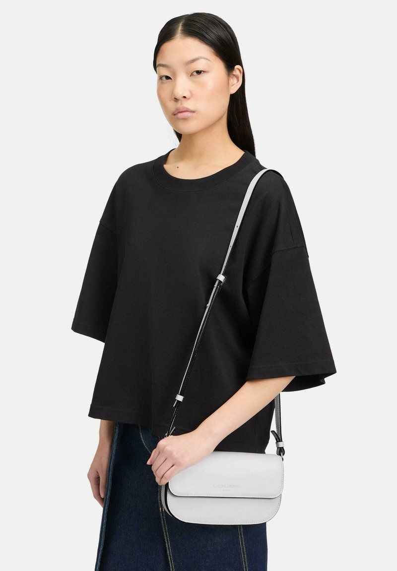 Czarny oversize t-shirt z szerokimi rękawami, zestawiony z małą białą torbą na ramię z klapą i regulowanym paskiem.