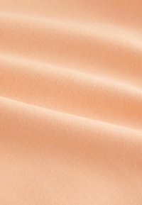 Tissu de couleur pêche avec une texture lisse, présentant des variations subtiles de lumière et d'ombre, mettant en valeur un motif de maillage doux et uniforme.
