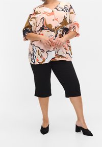 Blusa de botones multicolor con estampados florales y abstractos, mangas cortas, escote en forma de V, y pantalones capri negros. Combinada con tacones negros.