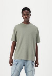 Olivgrön kortärmad texturerad T-shirt med rund halsringning, bärs med ljusblå cargojackor med flera fickor.