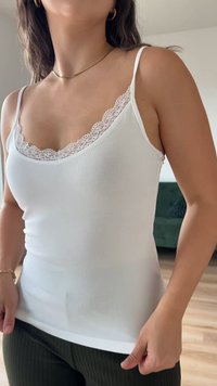Camisola branca de alças com um detalhe de renda ao longo do decote, alças finas e um corte ajustado, feita de um tecido liso e elástico.