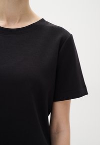 Černé tričko s krátkým rukávem a kulatým výstřihem, vyrobené z hladké látky. Jednoduchý design se švy na límci a rukávech.