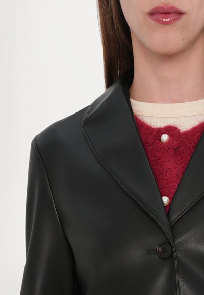 Black faux leather blazer with notched lapels and a single black button, layered over a red fuzzy sweater with pearl accents.