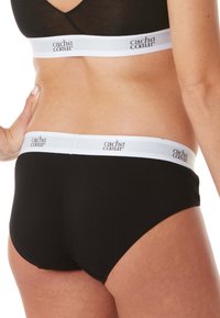 Schwarze Baumwollunterwäsche mit einem weißen Elastikbund, der mit "cache cœur" Branding versehen ist. Glatte Textur, mittelhoher Schnitt und volle Abdeckung.