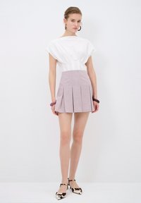Top blanco de manga corta con detalles fruncidos, combinado con una falda lavanda con pliegues. Complementado con zapatos de tacón de punta con estampado y tiras.
