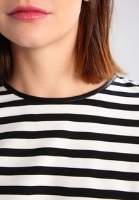 Černo-bílý pruhovaný top s kulatým výstřihem, který se vyznačuje hladkou, měkkou texturou a černým lemováním kolem límce.
