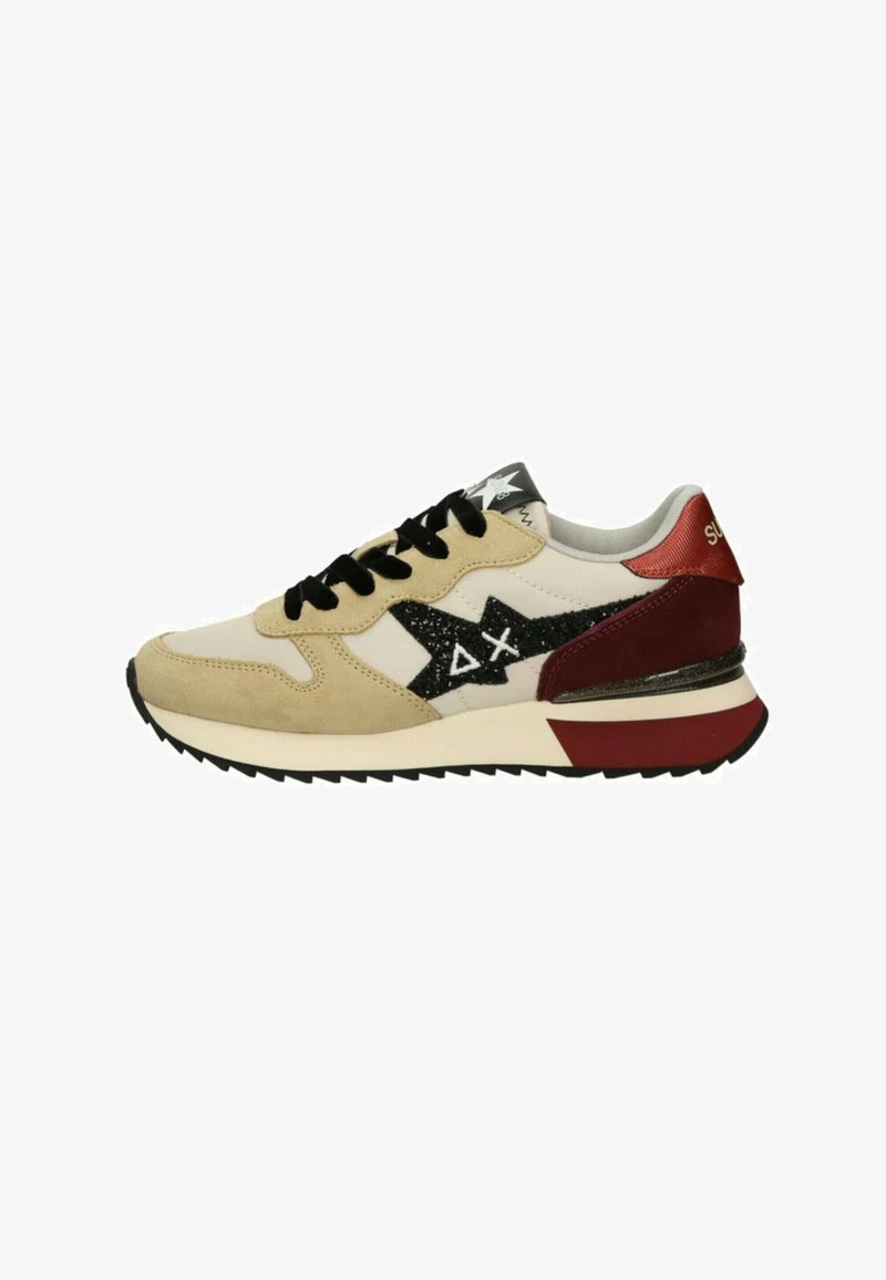 Baskets beige et blanches avec des lacets noirs, un logo étoile noir avec des symboles blancs, et des accents rouges sur le talon et la semelle.