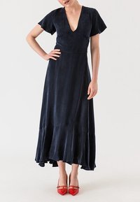 Námořnický modrý šaty po kotníky s výstřihem do V, volánkovými rukávy a skládanou sukní. Nosí se s červenými špičatými botami. Hladká textura látky.