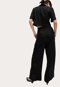 Blazer noir court avec des manches courtes et une découpe au dos, associé à un pantalon large taille haute. Tissu lisse avec une texture subtile.